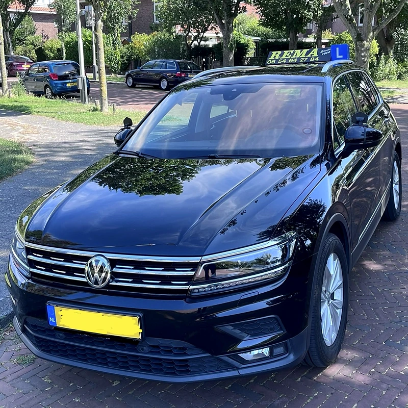 De lesauto van Rema Verkeersschool, een zwarte Volkswagen Tiguan met het blauwe dakbord